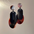 Dettaglio di orecchini pendenti in acrilico con motivi geometrici rosso e ambra - Ago in Argento-Nero-Caffè