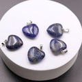 Five heart-shaped blue lapis lazuli pendants with silver clasps on white stand - Blue Sodalite