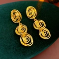 Detailed view of vintage gold spiral drop earrings on dark green velvet surface - Gold