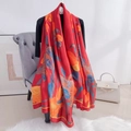 Sciarpa in seta rossa con stampe floreali blu e arancioni drappeggiata su sedia grigia - Rosso