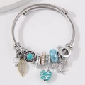 Bracciale a spirale argento con ciondoli cuore blu, farfalla e corona su fondo grigio - Blu
