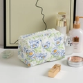 Quilted floral makeup bag in white with blue flowers and zipper on white table - Orchid and Green Leaves