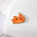 Süßer orangefarbener Emaille-Krabbenanhänger mit Goldkanten auf weißem Steinhintergrund - Orangefarbene Krabbe