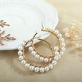 Detail of gold beaded hoop earrings with white pearls on a decorative white ceramic plate - White