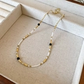 Detail of beaded necklace with white, gold, and black beads in a beige jewelry box - Black White Gold