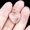 Hand holding a heart-shaped pink crystal pendant with a polished gold metal frame - Clear Quartz Gold Edging