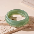 Close-up of translucent light green resin bangle with geometric facets on travertine stone - Green