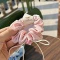Pink fabric scrunchie with button detail and white bow shown on a wooden background - Yorkie Tag Pink Button Bow Hair Tie