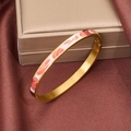 Nahaufnahme von Gold-Emaille-Armreif mit rosa-weißen Mustern auf braunem Seidenstoff - Bemalter Blumenstil / Rot + Hellviolett