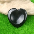 Polished black crystal worry stone heart on green grass and rock background - Obsidian