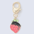 Detailed view of a cute black cat resting on a red strawberry metal keychain charm - Rose Red Strawberry Cat