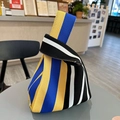 Knit knot wrist bag with yellow, blue, black, and white vertical stripes on a table - Striped Black