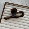 Macro detail of amber resin hair claw clip showing glossy twisted ring design on beige tray - Matte French Amber