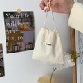 Close-up of corduroy drawstring bag with a minimalist logo tag in a cozy lifestyle setting - Milk White