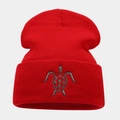 Detailed close-up of a red ribbed beanie featuring grey sea turtle embroidery texture - Red