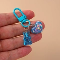 Close-up of blue gummy bear and glitter heart charm on light blue lobster clasp - Blue