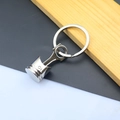 Polished metal piston keychain detail with circular keyring against a wood background - Wide Engine Piston / Silver