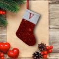 Detail of red sequined Christmas stocking with embroidered letter V on wood background - Letter V