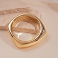 Detalle de brazalete cuadrado de oro pulido presentado sobre un soporte de piedra - Cuadrado Dorado