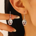 Gros plan de boucles d'oreilles crâne argenté vintage avec détails rouges portées - Visage aux yeux rouges (DZ-506) / Argent Antique