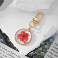 Porte-clés artisanal en résine avec fleurs séchées rouges et feuilles d'or en cadre doré - Fleur Rouge