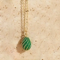 Green enamel egg-shaped pendant necklace with gold spiral wrap on a beige stone surface - Green