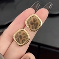 Quadratische Ohrstecker mit Leopardenmuster und Goldrahmen in einer Nahaufnahme an der Hand - Silberner Ohrstecker-Gold-Kaffee