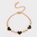 Detalle de pulsera de corazón dorada con dijes de esmalte negro y circonitas cuadradas - Dorado