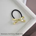 Detailansicht eines goldenen X-förmigen Haargummis mit schwarzem Seil auf einem Tablett - Gold Glänzend X-Form