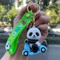 Close-up of a cute cartoon panda riding a blue scooter keychain with a green strap - Panda Gen 4 - Style 04