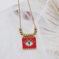Macro detail of Bohemian evil eye pendant with red beads and golden metal accents - Orange