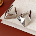 Macro shot of silver geometric metal earrings with a polished finish on a linen book - Silver
