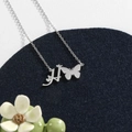 Polished stainless steel letter necklace with butterfly charm on a blue velvet pad - Silver H