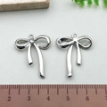 Silver bow knot alloy pendants with rhinestones shown against a wooden ruler for size - Rhinestone Bowknot - Silver (21395)