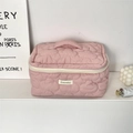 Close-up of pink quilted makeup bag featuring heart patterns and woven brand label - Pink