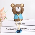 Detail of cute resin bear figurine in blue suit with long rope legs sitting on books - See-no Bear