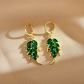 Detail view of gold earrings featuring green leaf-shaped crystals on elegant silk background - Green