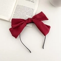 Detail view of a large red satin bow headband on an open book over white background - Wine Red (Headband)