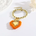 Detail der Herz-Halskette mit Flammenkrone und polierten goldenen Perlenarmbändern - Orange
