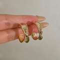 Handheld view of elegant twisted gold-tone C-shape earrings with a polished mirror finish - Twisted C-hoop Gold