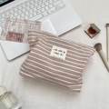 Top view of striped toiletry bag with sozakka beauté label among lifestyle desk props - Brown White