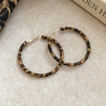 Close-up of C-shaped leopard print hoop earrings with leather wrap on fabric background - Brown - 5cm