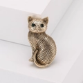 Vintage cat brooch in antique gold finish with emerald green gemstone eyes on white stand - Gold