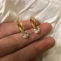 Detail of gold hoop earrings with sparkling zircon stones held on a fingertip - 925 Silver / Gold