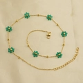 Detailed view of the gold chain bracelet featuring green beaded flower charms on fabric - Green Necklace Style