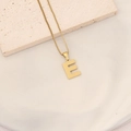 Macro shot of textured gold letter E pendant on a matching box chain over stone - Letter E