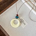 Close-up of cream resin circular pendant with amber and teal beads on brown wax cord - Round Pendant / Cream White