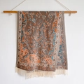 Ethnic paisley shawl with fringe in brown blue and orange tones hanging on a wooden rod - Brown