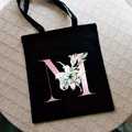 Black canvas tote bag featuring pink letter M print and lily flower pattern design - Letter M / Black
