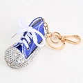 Detalle de llavero de zapatilla de lona azul con pedrería brillante y accesorios en tono dorado - Azul
